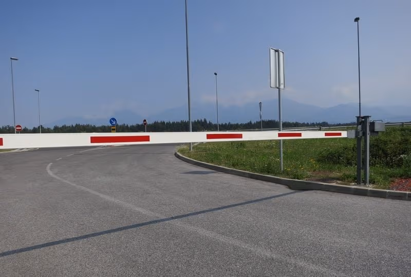 Ručna putna rampa sa crveno-belom rukom preko asfaltiranog prolaza.